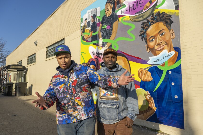 Muralists Pugs Atomz and Damon Lamar Reed stand next to a mural they both worked on in Grand Crossing.