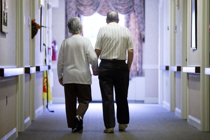 An elderly couple walks down a hall.