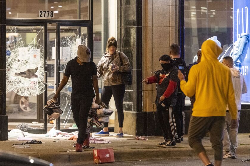 Onlookers watch as a looter walks away with dozens of shoes stolen from a Foot Locker in Logan Square, Friday night, May 31, 2020.