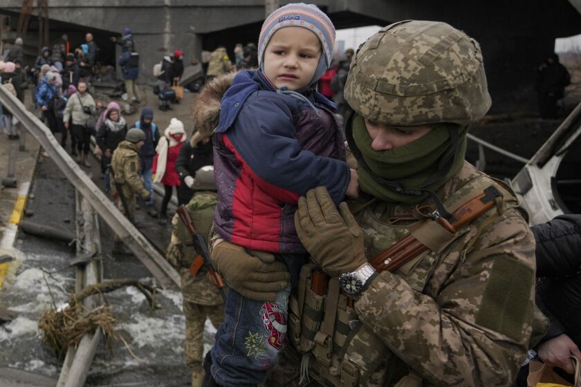 A Ukrainian serviceman holds a baby crossing the Irpin river Saturday on an improvised path under a bridge that was destroyed by a Russian airstrike.