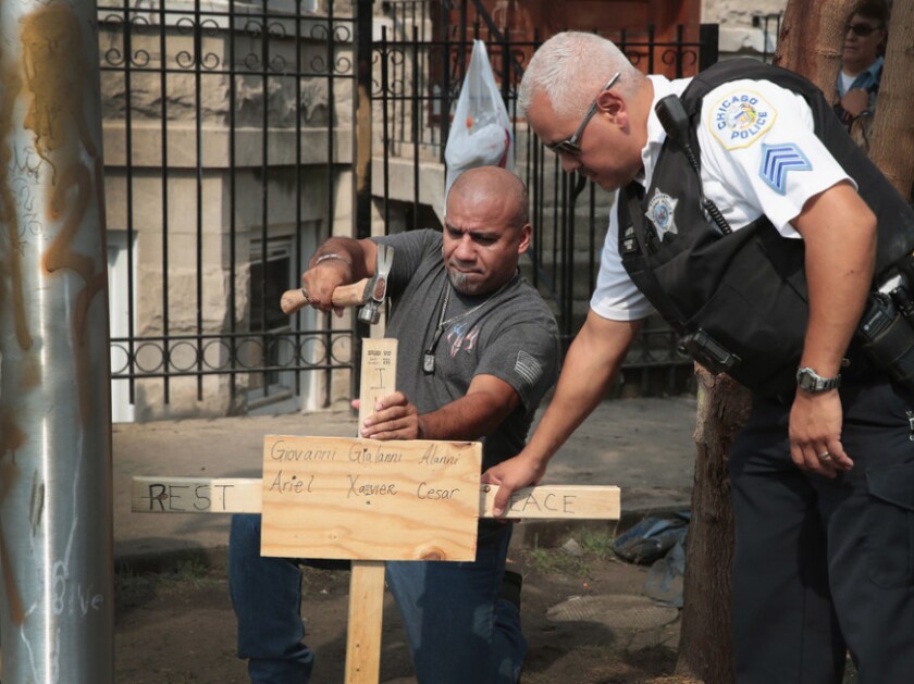 A Chicago police officer helps as Omar Acevedo pounds a cross bearing the names of victims into the dirt outside the Little Village building where a fire killed 10 children last month. | Getty Images