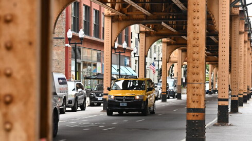 A yellow Chicago taxicab minivan driven by Bob Singh travels beneath elevated CTA train tracks on Tuesday, June 16, 2026.