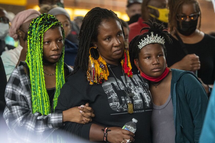 Keinika Carlton (center) daughter of Keith Cooper, comforts her daughters Alyna Carlton, 17 (left), and Mikayla Carlton, 11, during a memorial and candlelight vigil for her father at Kimbark Plaza, 53rd Street and Kimbark Avenue on Friday night., July 16, 2021. Keith was punched in the head and killed during a attempted carjacking in the plaza earlier in the week.