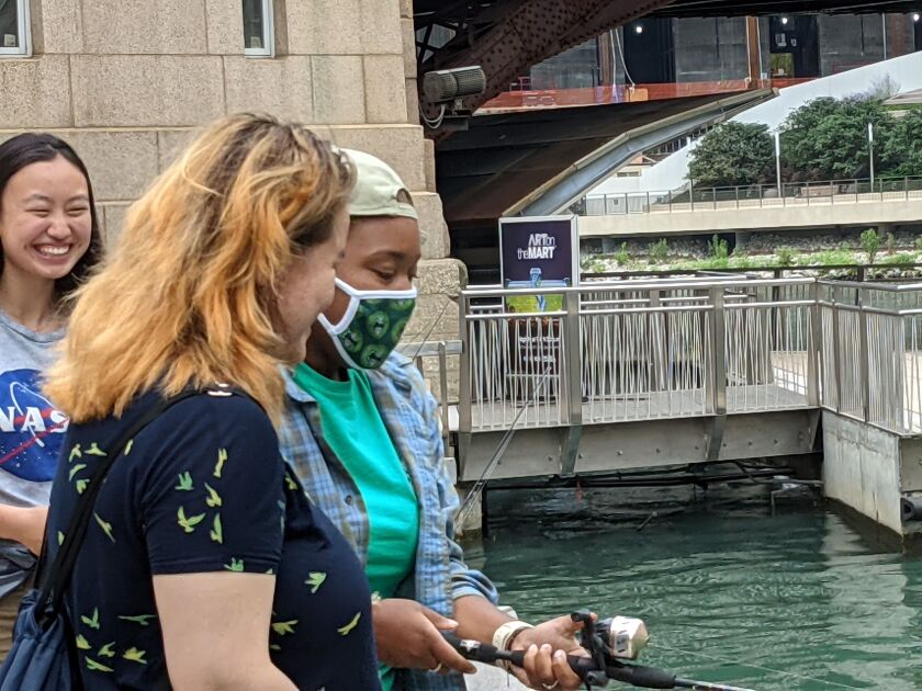 Destiny Berry (with mask) teaches a visitor to “Fishing at the Jetty” the basics of fishing from the Chicago Riverwalk. Credit: Dale Bowman
