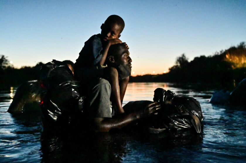 A man carries a child on his shoulders as Haitian migrants cross the Rio Grande river between Ciudad Acuna, Coahuila state, Mexico, and Del Rio, Texas, on Sept. 23, 2021.