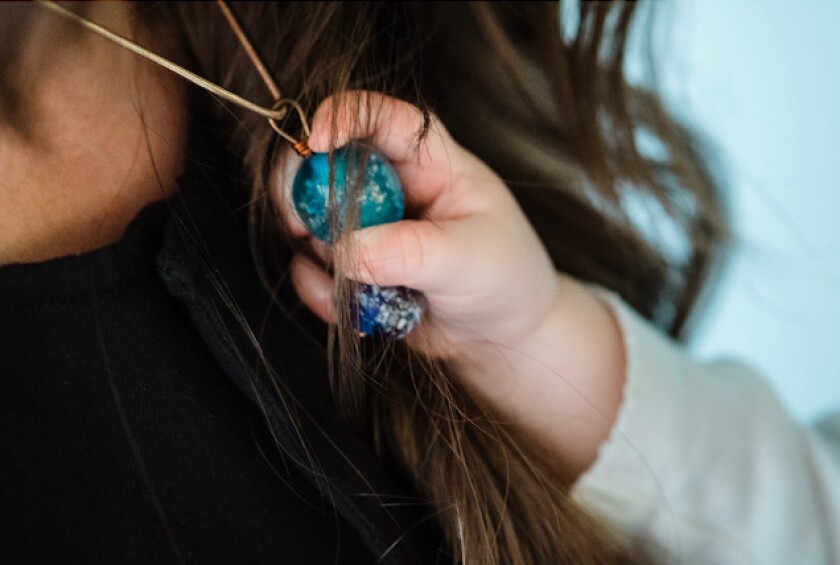 A pendant created for Roberta and Sean Scott with some of the ashes of their infant son Arrow, who died at birth. Their daughter Sparrow reaches out and touches the blown-glass jewelry.