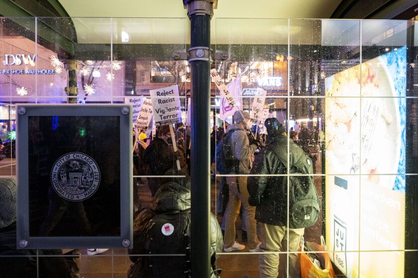 Three people waiting at a State Street bus stop watch protesters march past on Friday, Nov. 19, 2021. They were protesting the acquittal of Kyle Rittenhouse.