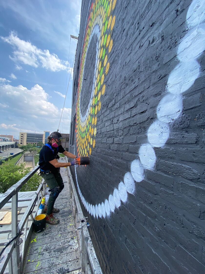 Joe Miller sprays paint through an empty paint can to create the dots for “Uptown Dot King” at 1124 W. Wilson St.