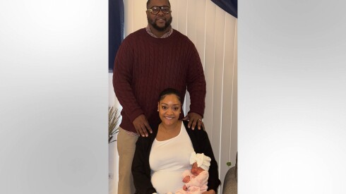 Mercedes Wells holds her newborn daughter, Alena Wells, as her husband, Leon Wells, stands behind them.