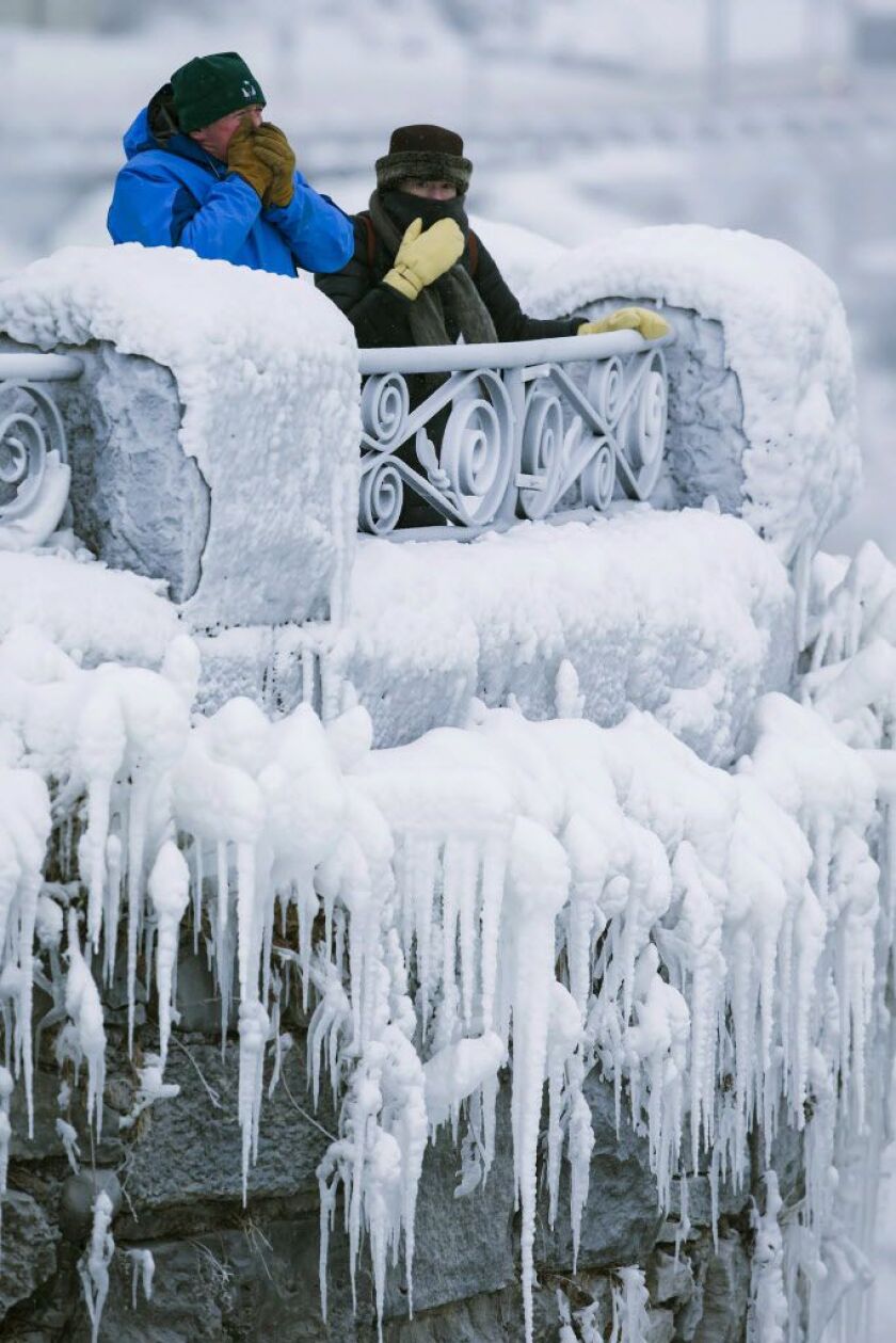 Visitors try to keep warm at the brink of the Horseshoe Falls in Niagara Falls, Ontario, as cold weather continues through much of the province on Friday, Dec. 29, 2017. (Aaron Lynett/The Canadian Press via AP)