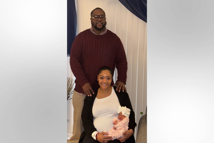 Mercedes Wells holds her newborn daughter, Alena Wells, as her husband, Leon Wells, stands behind them.