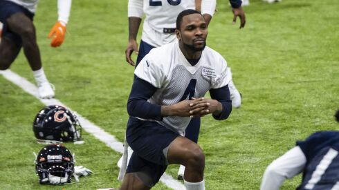 Bears safety Eddie Jackson stands on a grass field and stretches with his legs crossed.