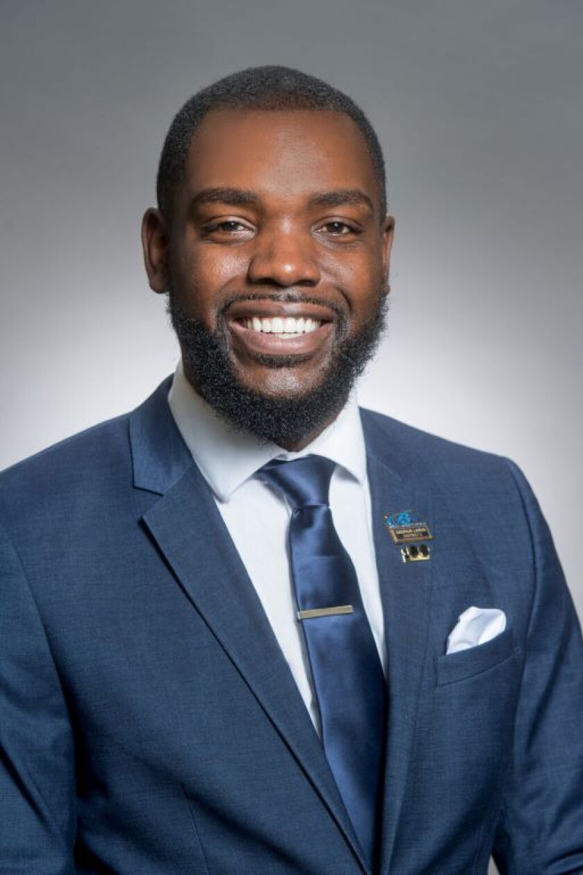 A Black man wearing a blue suit and tie with a pocket square.