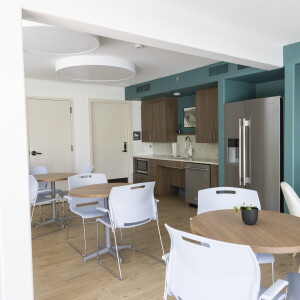A community room with chairs, tables and small kitchen space.