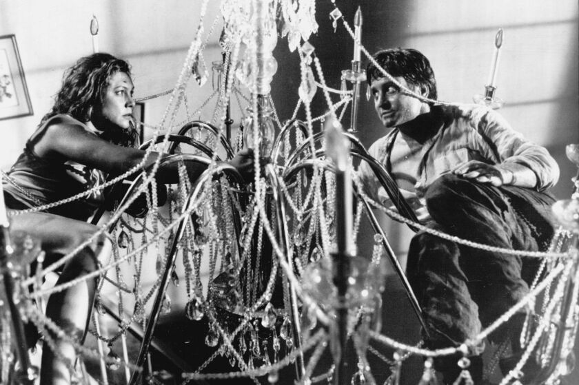 Kathleen Turner and Michael Douglas star as a violently feuding couple in the dark comedy “The War of the Roses.” Turner did many of her own stunts, including jumping from a second-floor landing onto a massive chandelier.