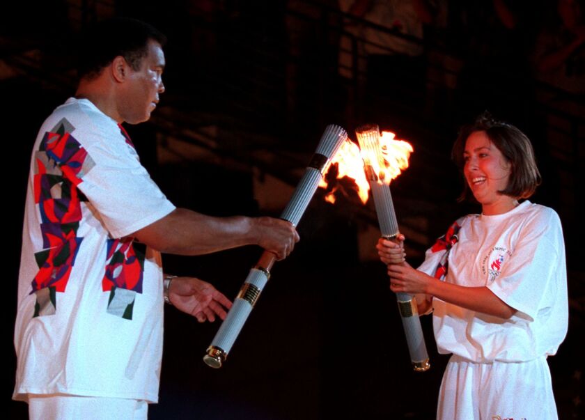 American swimmer Janet Evans passes the Olympic flame to Muhammad Ali during the 1996 Summer Olympic Games Opening Ceremony in Atlanta on July 19, 1996.