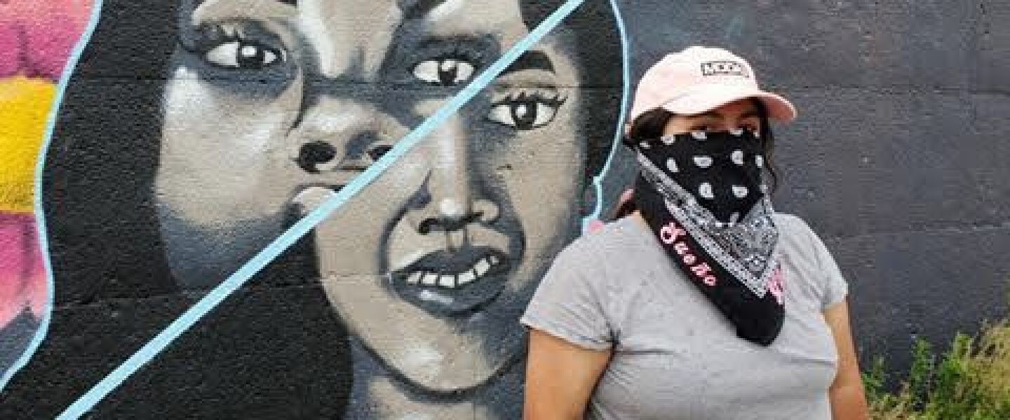 Artist Sueño in front of her mural combining the faces of Breonna Taylor and Vanessa Guillén, painted on the cinderblock wall this summer at Splash 2020.