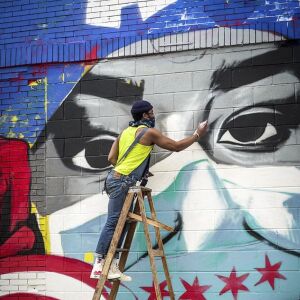 Artist Dwight White II works on a mural on the side of Lulu’s Hot Dogs inspired by a neighbor who is a nurse.