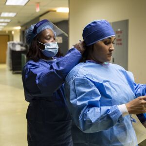 Registration clerk Frances Horton assists nurse practitioner Capri Reese with her personal protective equipment at Roseland Community Hospital on the Far South Side, Tuesday afternoon, April 28, 2020. During Reese’s 12-hour shift Tuesday, she responded to five code blues, meaning the patient’s heart stopped beating, and three patients died.