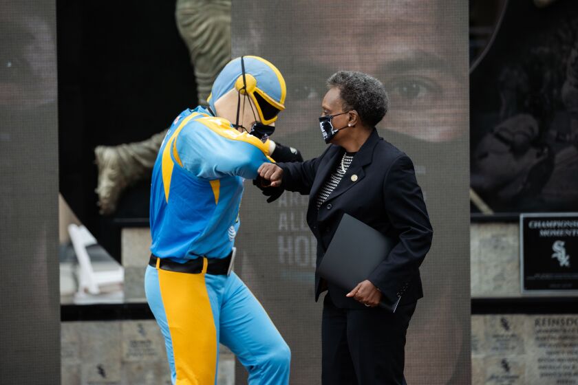 Chicago Mayor Lori Lightfoot bumps elbows with Sky Guy, mascot of the WNBA’s Chicago Sky, during a press conference at Guaranteed Rate Field on Tuesday. Lightfoot launched an awareness campaign, using local sports teams, called “We Are All One Team” that encourages young people to wear masks, maintain social distance and stop gathering in large groups to help prevent the spread of COVID-19.