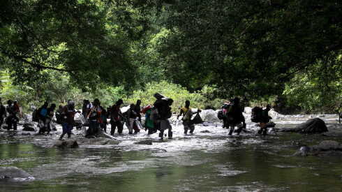 Migrants holding their belongings in their hands and on their backs walk in a river as they trek through the infamous Darien Gap on their journey towards the United States.