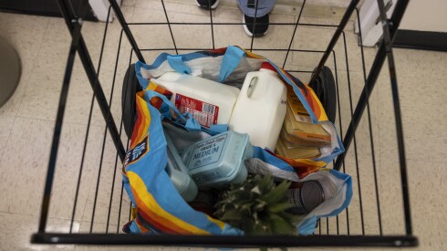 Un carrito de compras negro con leche y otros comestibles.