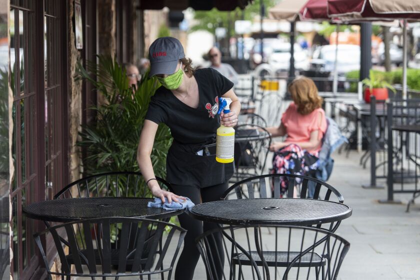 Emily Cribbin, a server at Poor Phil’s in Oak Park sanitizes a table for a customer in May.