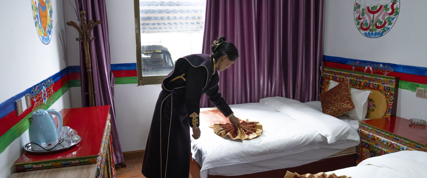 A woman in ethnic dress adjusts a bedspread at her tourist homestay in Zhaxigang village near Nyingchi in western China’s Tibet Autonomous Region.