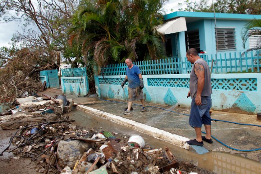 Two men wash away mud and debris from the front of their house in the aftermath of Hurricane Maria in Arecibo, Puerto Rico. | Ricardo Arduengo/AFP/Getty Images
