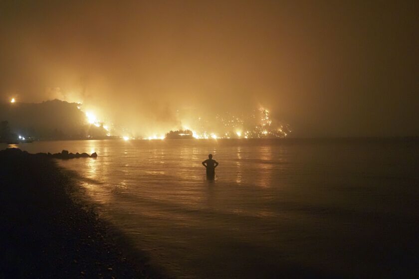 In this file photo dated Friday, Aug. 6, 2021, a man watches as wildfires approach Kochyli beach near Limni village on the island of Evia, about 160 kilometers (100 miles) north of Athens, Greece.