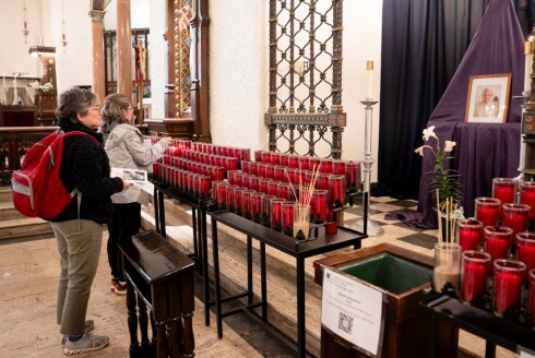 Renee Blanchard (in grey) and Deborah De Rosa light a candle and stand in silence near an altar for Pope Francis at St. Thomas the Apostle Church in Hyde Park, Saturday, April 26, 2025.