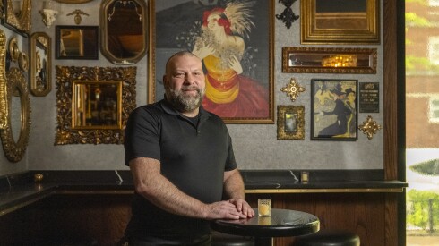 A man stands in front of a wall covered with mirrors and framed posters