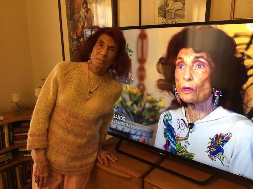 Zelda Sands standing in front of a TV playing a documentary for which she was interviewed, “Lady You Shot Me: the Life and Times of Sam Cooke.”