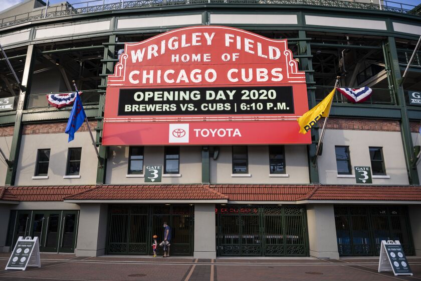 Fans walk by closed gates at Wrigley Field shortly before the start of the opening day game between the Chicago Cubs and the Milwaukee Brewers, Friday evening, July 24, 2020.
