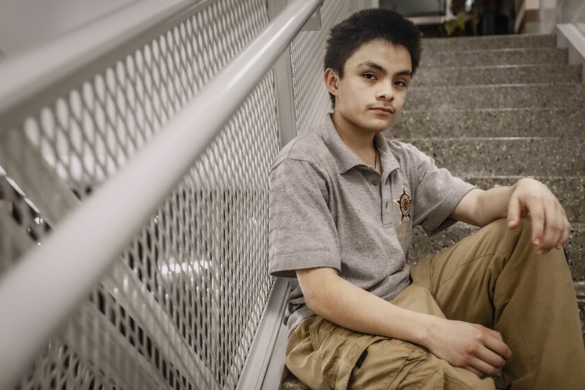 A teen with brown spiky hair wearing khakis sits in the stairwell of his school.
