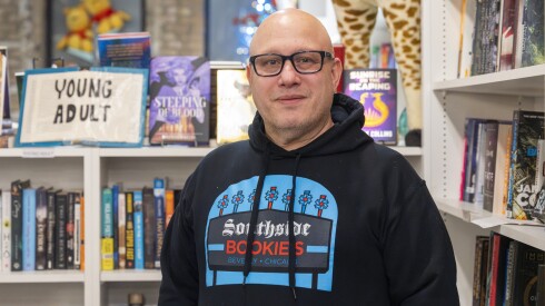 A man with glasses stands in front of book shelves in a bookstore.