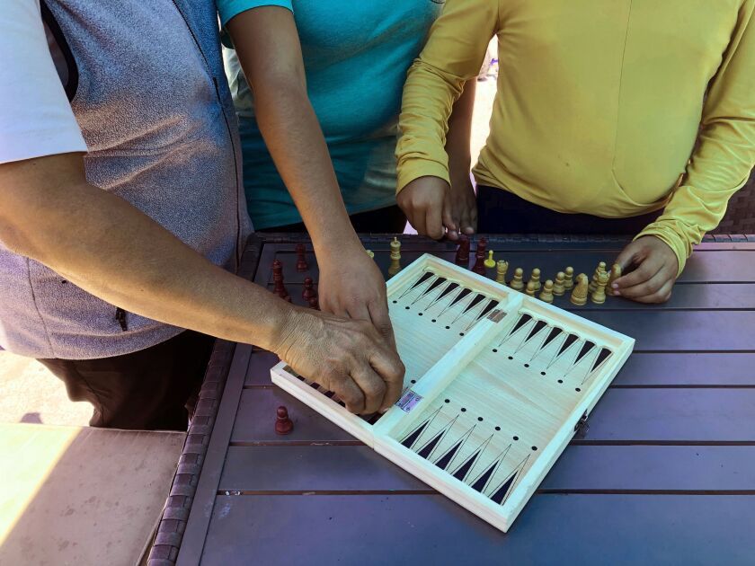 (From left) Luz Viviana Perez, 53, arranges a chess board with her daughters, 17 and 12. at a migrant shelter in San Diego where the family, from Mexico, is seeking asylum.