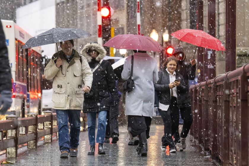 Groups of people using umbrellas to shield themselves from rain and snow cross the DuSable Bride, in the Streeterville neighborhood, as Chicago and surrounding communities are under a winter weather advisory, Tuesday, Jan. 9, 2024.