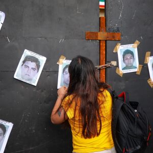 A woman puts photos of missing students on a wall on Sept. 26, 2022 outside the Palacio Nacional in Mexico City to commemorate the eighth anniversary of their disappearance.