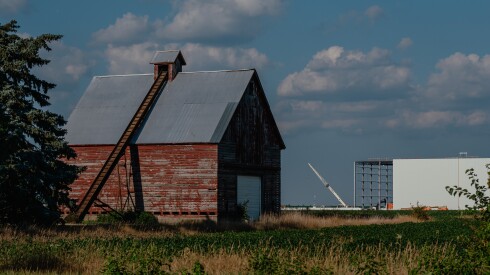 An industrial building can be seen rising in the distance among old farmhouses and rows of corn near CenterPoint in Joliet The ongoing construction of CenterPoint’s massive logistics and intermodal facilities has drawn controversy for its placement in historically rural and agricultural areas, where residents have complained about increased truck traffic, environmental impacts and the transformation of farmland into industrial zones.