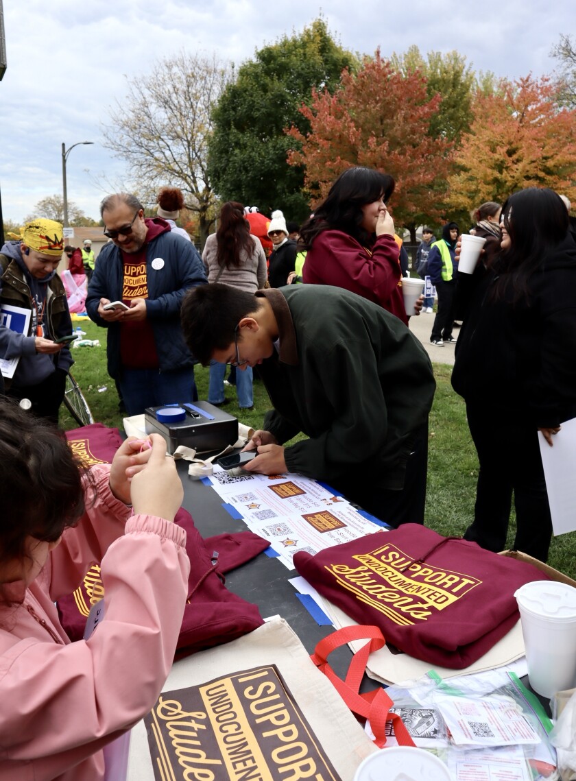 A person wearing a light black jacket pays for a maroon sweatshirt that says "I support undocumented students."