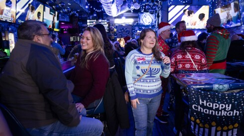 Becky Adelberg wears a sweater with a menorah pattern at 8 Crazy Nights, a Hanukkah-themed bar in Lake View, Saturday, Dec. 13, 2025.