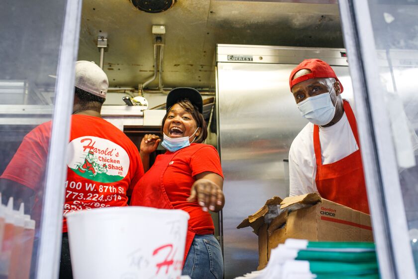 Cashier Jessica Jarmon (center) and cook Hubert Key (right) smile inside the Harold’s Chicken food truck, at the Daley Plaza, Friday afternoon, Oct. 15, 2021. They said they enjoy the fast-paced atmosphere of working in a food truck.