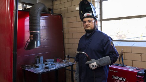Man in blue jumpsuit holds a welding torch.