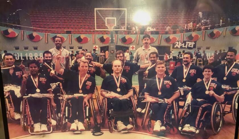 The U.S. Men’s Wheelchair Basketball Team won gold at the 1988 Paralympics in Seoul. Mustachioed head coach Frank Burns is seen standing, right. David Kiley is in the front row, signalling the team is “No. 1.”