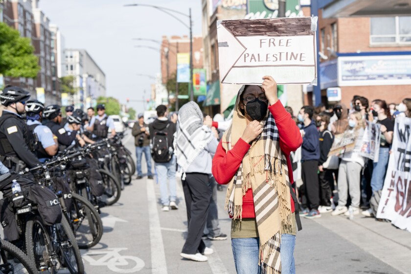 A protesters holds a sign that reads, “Free Palestine” as police officers form a barricade with their bikes across the street from DePaul University in Lincoln Park, hours after Chicago police cleared the pro-Palestinian encampment on campus early Thursday, May 16, 2024. | Pat Nabong/Sun-Times