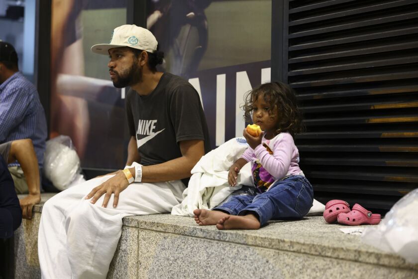Cataleya takes a bite of a nectarine next to her father, Elier, as they wait for a bus to take them from Union Station to a refugee center Wednesday night, Aug. 31, 2022.