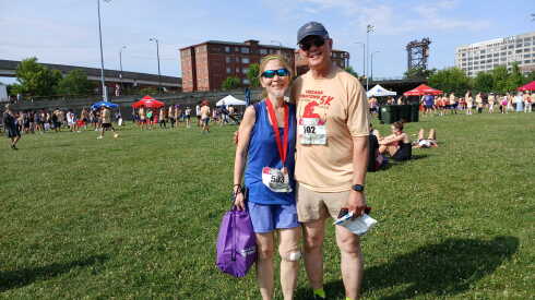 A man and woman in summer running clothes stand on a green lawn.