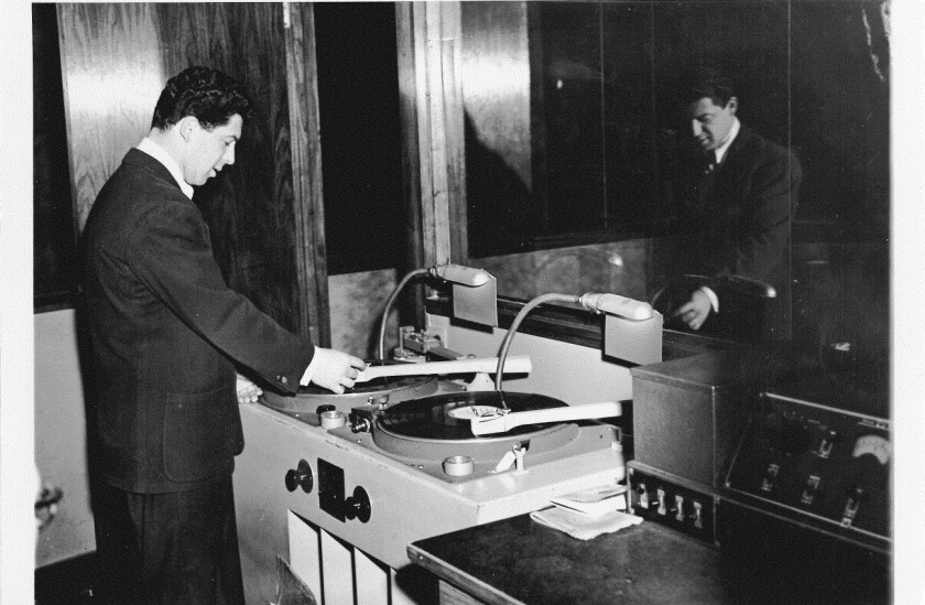 A man in a suit stands by a record player.