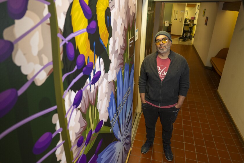 Artist Caesar Perez of Pilsen stands next to one of his murals in the main hallway of the Lakeview North Clark Street Health Clinic.